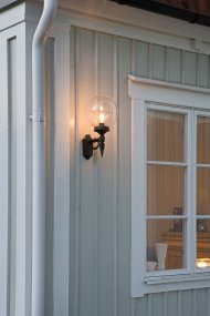 Orion Svart från Konstsmide - Med sina dekorativa detaljer och tidl&ouml;sa stil blir denna v&auml;gglampa en elegant detalj som lyfter din fasad och skapar en inbjudande atmosf&auml;r.