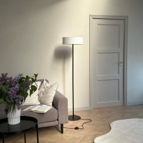 Calix Svart golvlampa från Dyberg Larsen - Med sin slanka, svarta metallstomme och en elegant, vit lampsk&auml;rm sprider den ett behagligt och mjukt ljus i rummet.