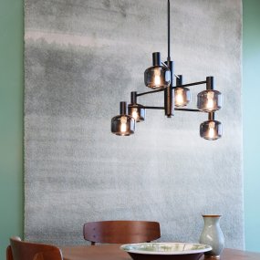 Arp Ø50 Svart taklampa från Dyberg Larsen - Skapa perfekt balans mellan form och funktion med Arp ljuskrona, som har 6 vackra glaskupor i r&ouml;kf&auml;rgat glas och en elegant svart upph&auml;ngning.