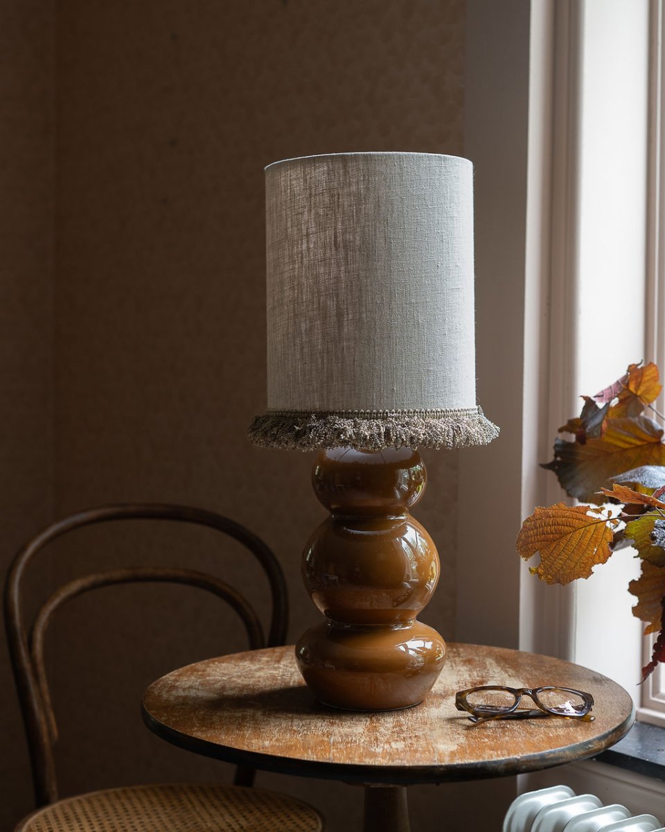 Lampskärm Cylinder Frans Ø22 Natur från Alde & Lind - Kanterna &auml;r omsorgsfullt invikta och l&auml;ngs nederkanten l&ouml;per en dekorativ, kraftig sn&ouml;rmakerifranskant som ger lampsk&auml;rmen en elegant och exklusiv detalj.