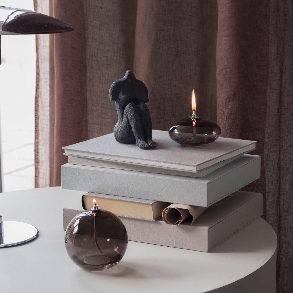 Oljelampa Aura Liten Rökfärgad från Mette Ditmer - Dess eleganta design och r&ouml;kf&auml;rgade glas sprider ett mjukt, varmt ljus som ger en lugn och mysig k&auml;nsla.