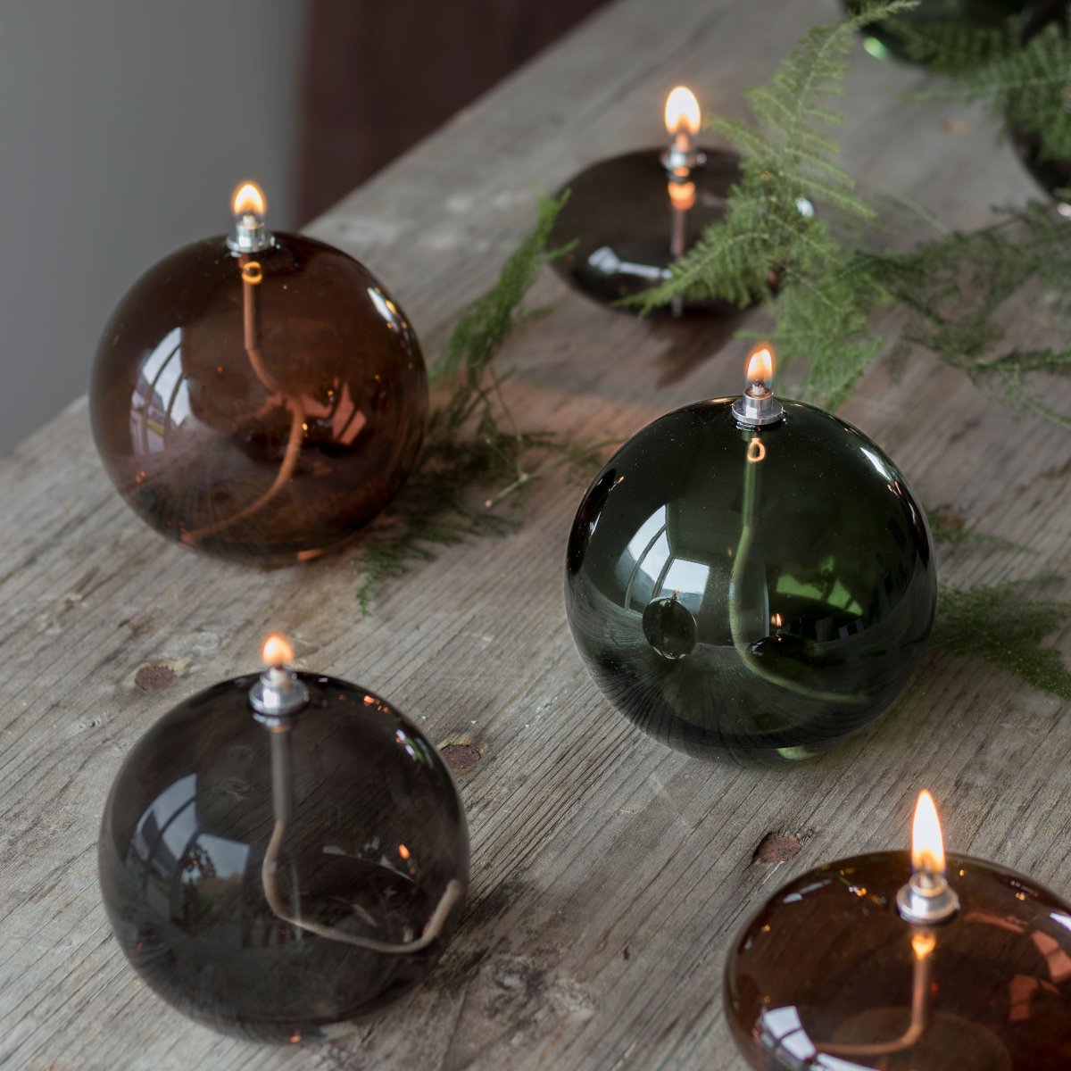 Oljelampa Aura Mellan Rökfärgad från Mette Ditmer - Dess eleganta design och r&ouml;kf&auml;rgade glas sprider ett mjukt, varmt ljus som ger en lugn och mysig k&auml;nsla.