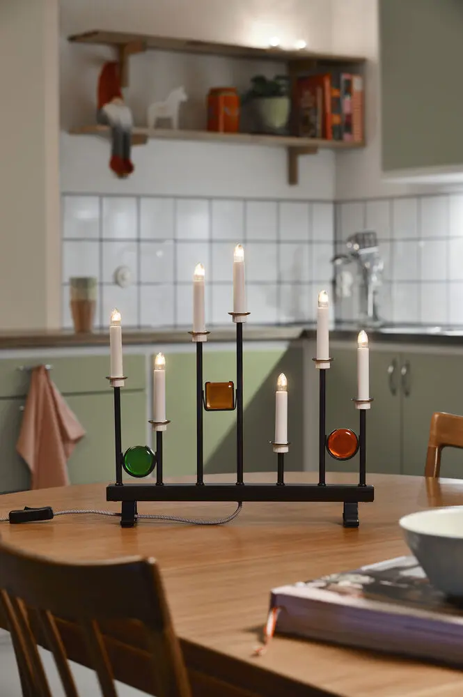 Elljusstake 7ljus Svart från Konstsmide - De sju ljusen ramas in av dekorativa f&auml;rgade glasdetaljer i gr&ouml;nt, r&ouml;tt och b&auml;rnstensgult, vilket skapar en elegant och festlig atmosf&auml;r.