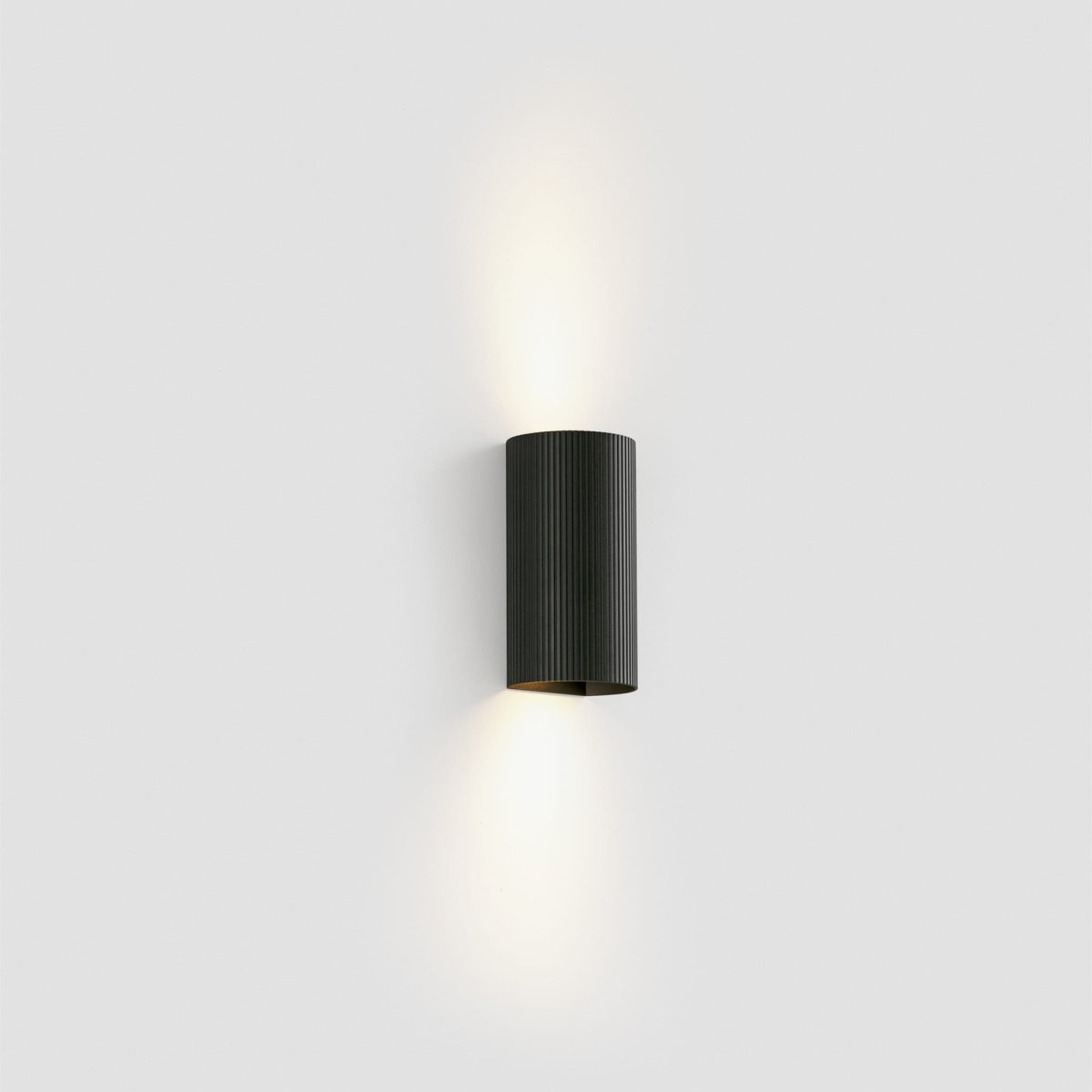Sole 15cm Svart räfflad vägglampa från Faro Barcelona - Den finns i tv&aring; storlekar och kan avge ljus i en eller tv&aring; riktningar, vilket g&ouml;r den idealisk f&ouml;r hallar och mindre utrymmen.