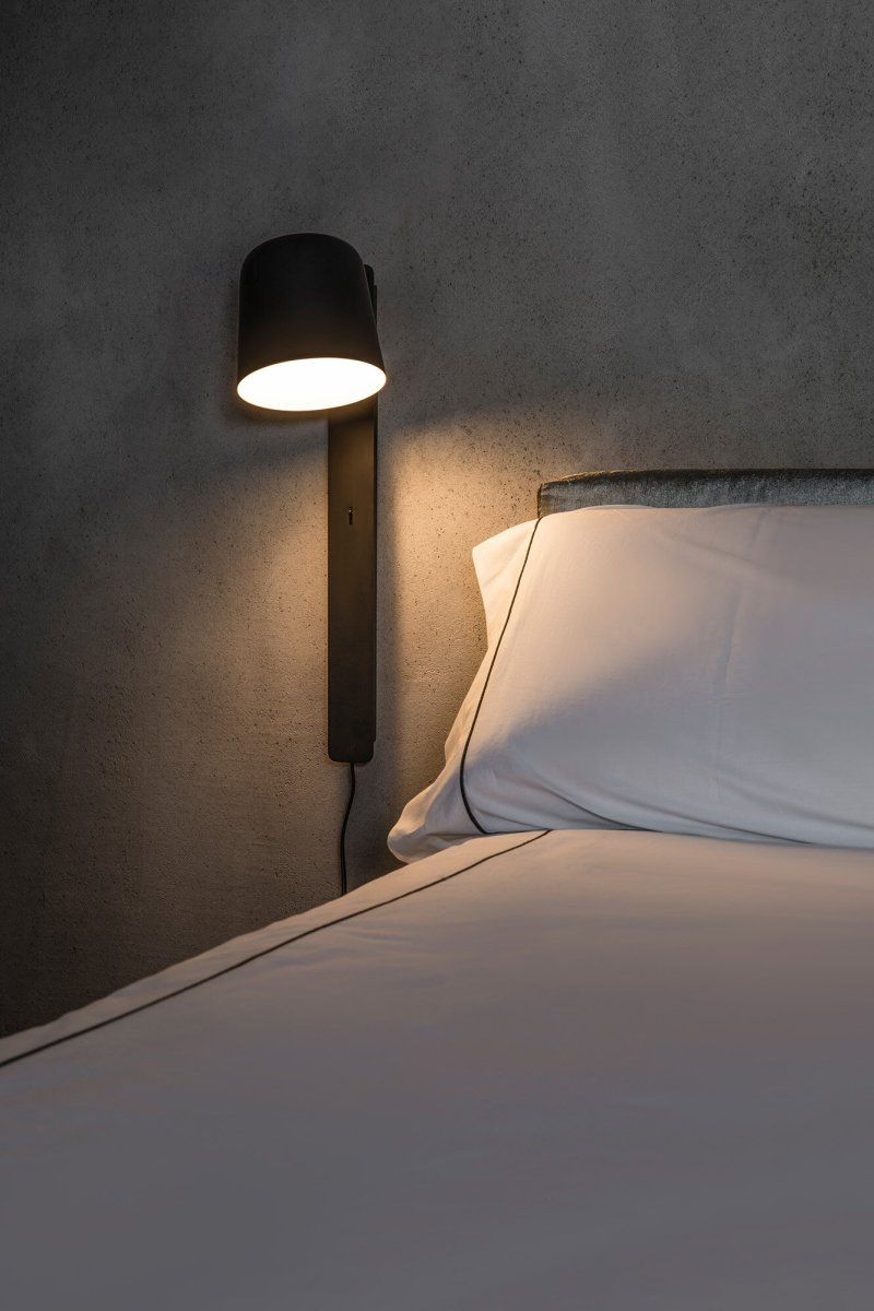 Tila 46cm Svart läslampa från Faro Barcelona - Den svarta st&aring;lstrukturen i nordisk stil rymmer inte bara en fullt justerbar ljusk&auml;lla, utan fungerar &auml;ven som praktisk hylla f&ouml;r en bok eller tidskrift.