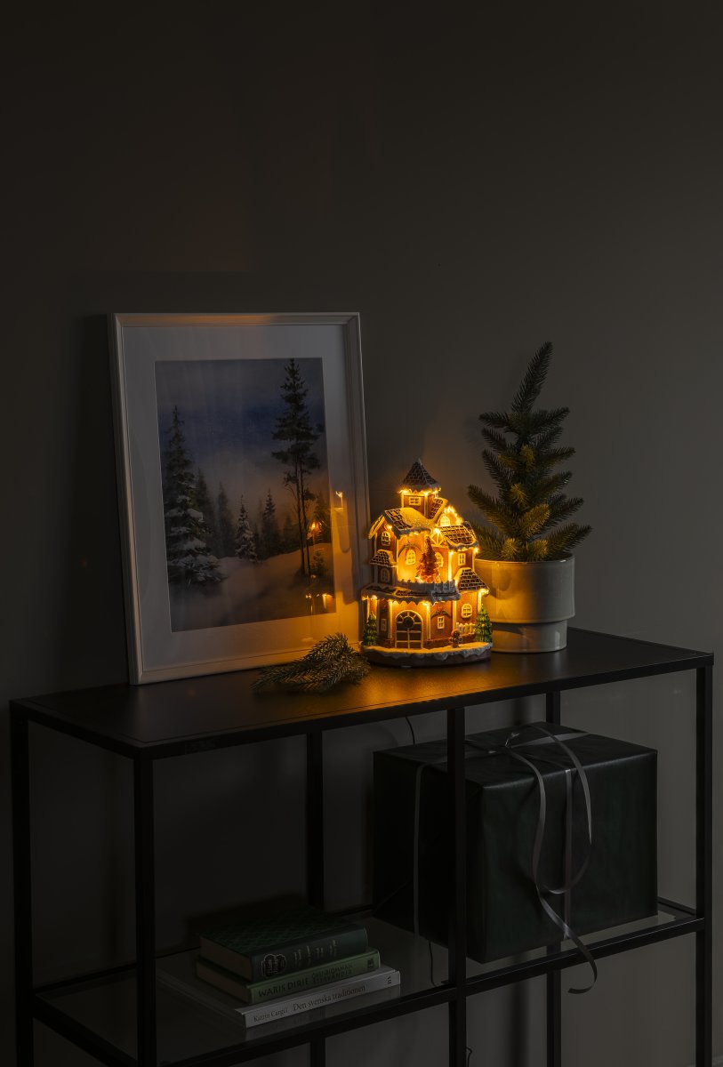 Pepparkaksby 30cm Brun från Konstsmide - Det detaljrika huset med sn&ouml;t&auml;ckta tak, lysande f&ouml;nster och dekorerad gran sprider ett varmt och inbjudande sken i rummet.