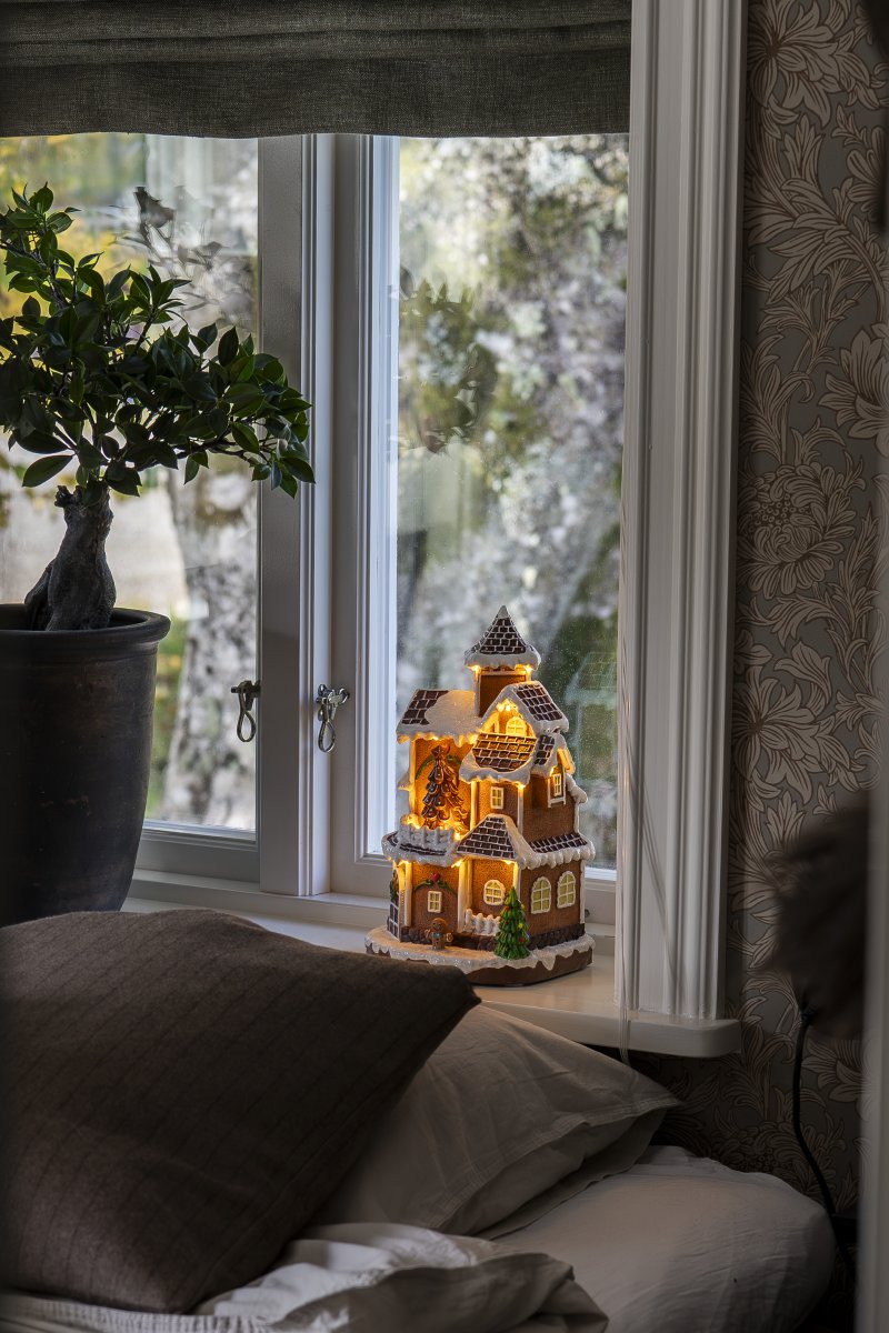 Pepparkaksby 30cm Brun från Konstsmide - Det detaljrika huset med sn&ouml;t&auml;ckta tak, lysande f&ouml;nster och dekorerad gran sprider ett varmt och inbjudande sken i rummet.