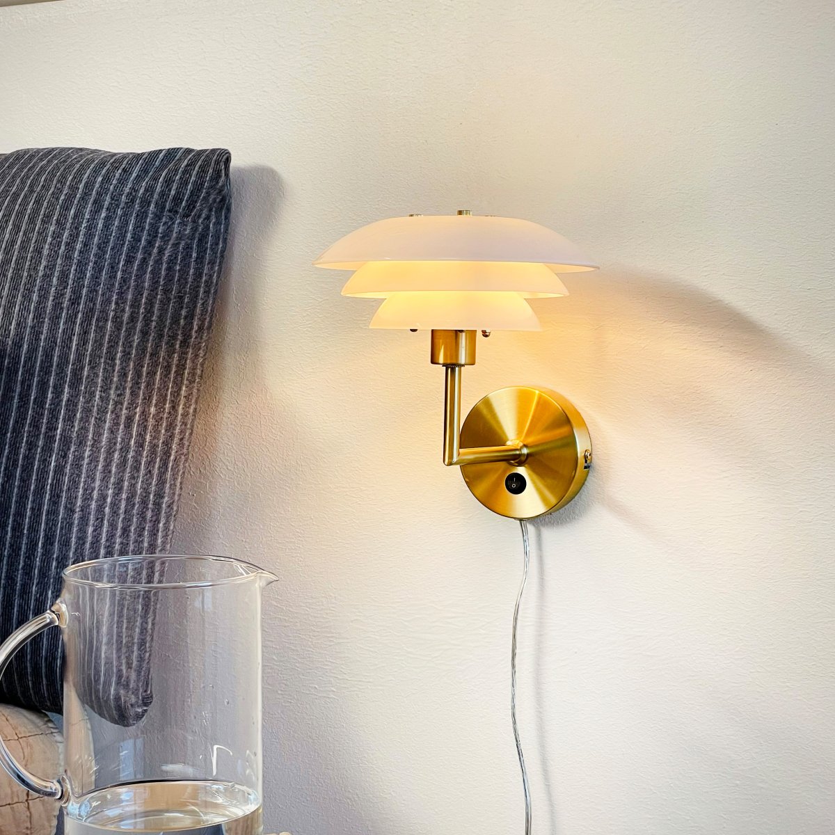 DL20 Mässing vägglampa från Dyberg Larsen - De tre lager av opalvita sk&auml;rmar sprider ett mjukt och j&auml;mnt ljus, vilket g&ouml;r den idealisk f&ouml;r att skapa en varm och inbjudande atmosf&auml;r.