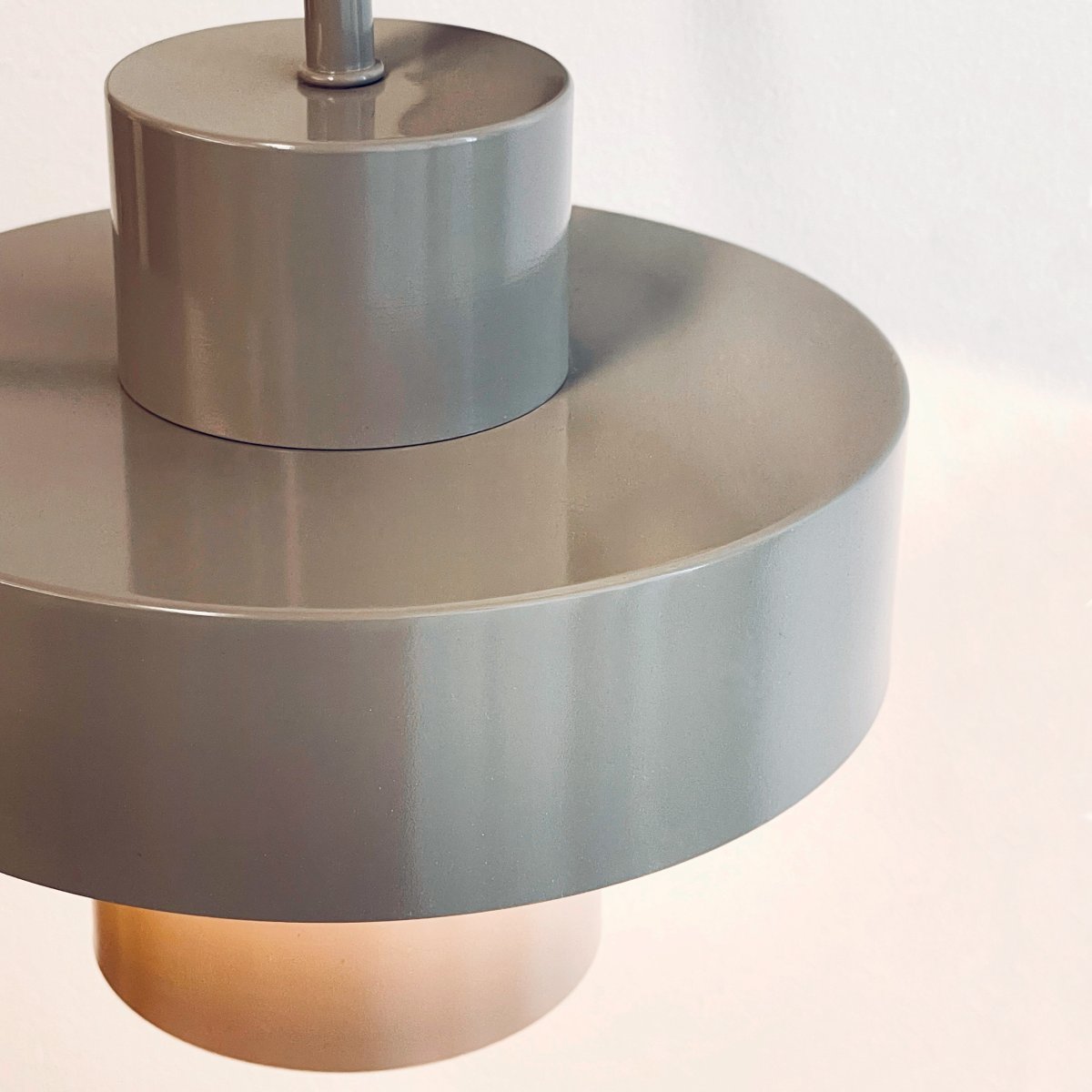 Stoke Ø15 Varmgrå vägglampa från Dyberg Larsen - Den &auml;r tillverkad i metall med en glansig yta som framh&auml;ver lampans cylindriska former och skapar en balanserad kontrast mot andra material som sten, tr&auml; och textilier.