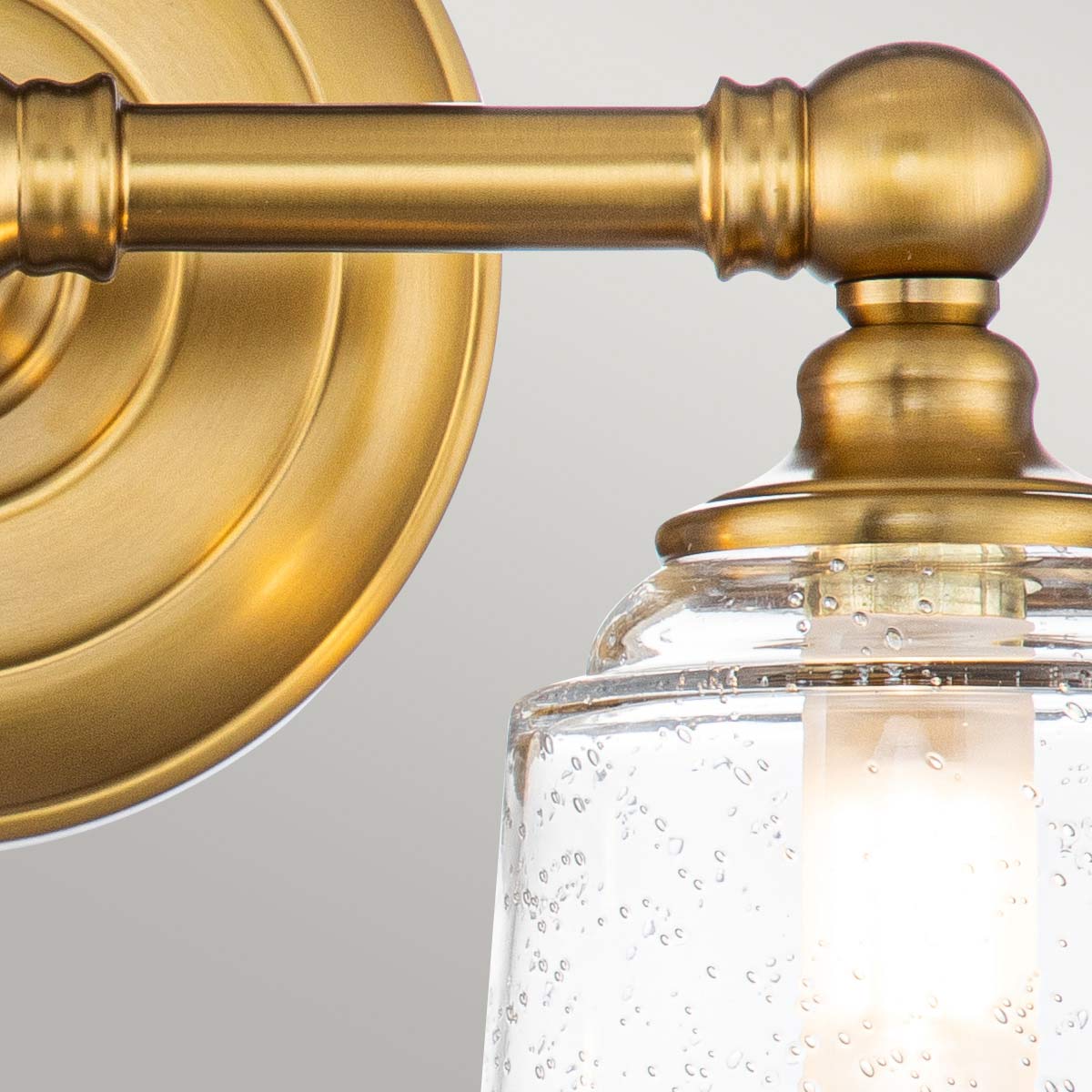 Huguenot Lake 33cm Mässing badrumslampa från Elstead Lighting - Den eleganta cirkul&auml;ra detaljen och handslipade f&auml;sten ger en k&auml;nsla av traditionell hantverkskonst, medan de klara, strukturerade glasen skapar ett mjukt och inbjudande ljus.