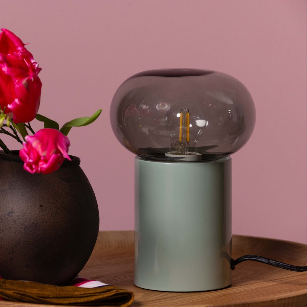 Knut 22cm Grön bordslampa från Brilliant - Den gr&ouml;na lampfoten ger ett fr&auml;scht och levande uttryck, medan den r&ouml;ktonade glaskupan skapar en mjuk och st&auml;mningsfull ljusspridning.