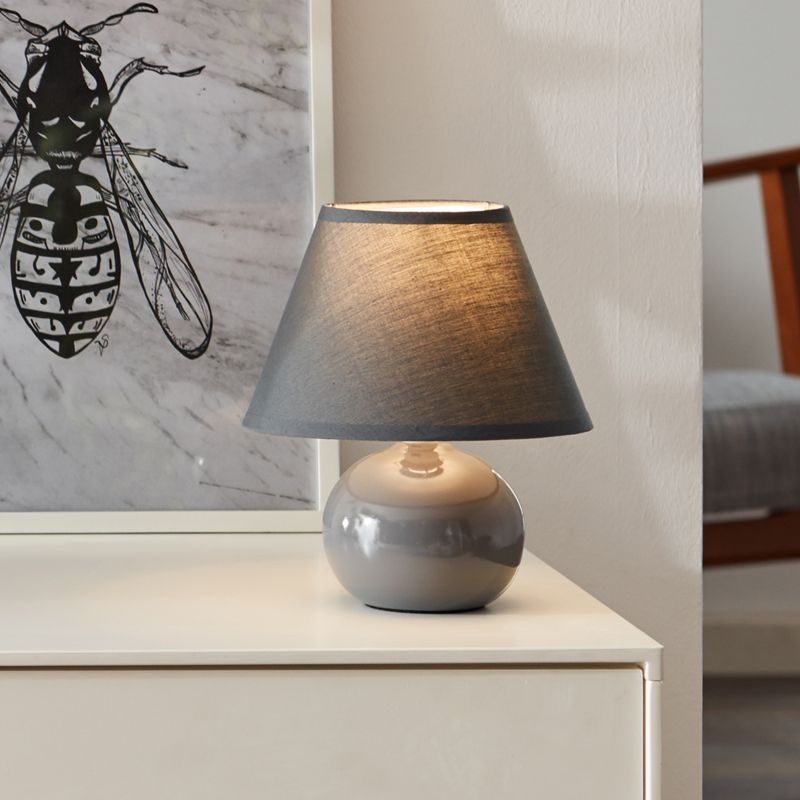 Primo 23cm Mörkgrå bordslampa från Brilliant - Den &auml;r tillverkad av textil och keramik och ger ett behagligt ljus.